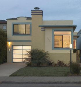White aluminum full-view garage door with frosted glass on two-story yellow home at dusk
