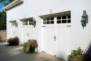 White vertical-panel carriage-style garage doors with upper windows on brick home