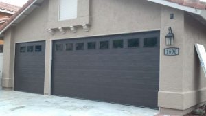 Charcoal raised-panel steel garage door with upper windows on tan stucco home
