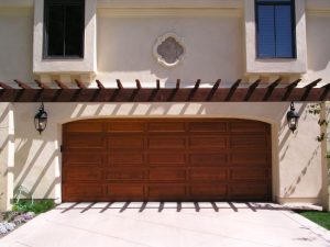 Dark walnut raised-panel wood garage door under pergola on stucco home